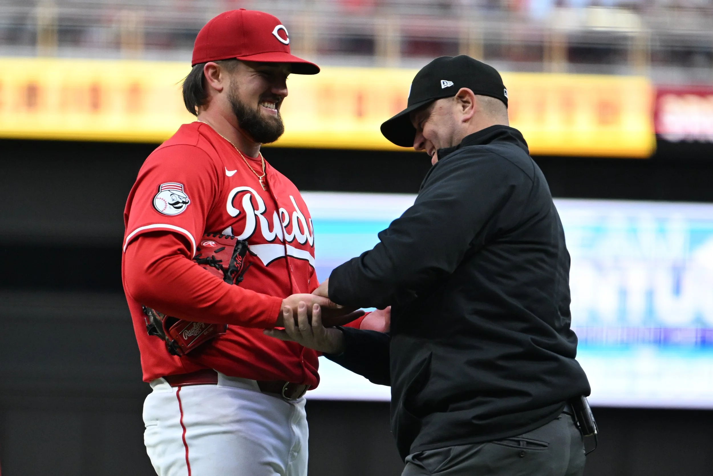 A baseball player in a red Cincinnati Reds uniform is smiling while receiving an award or plaque from a man dressed in black during a game or event.