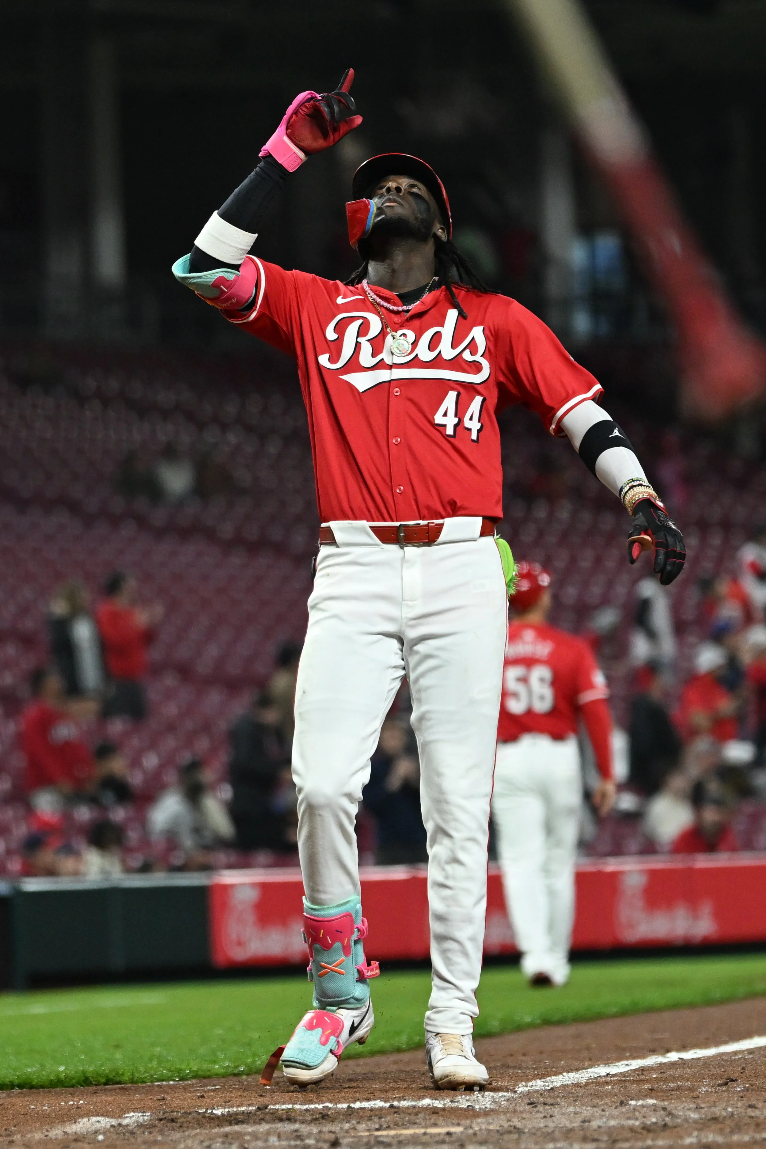 A baseball player from the Cincinnati Reds celebrating on the field, wearing uniform number 44, with a glove on his left hand, and his right hand raised pointing upward.