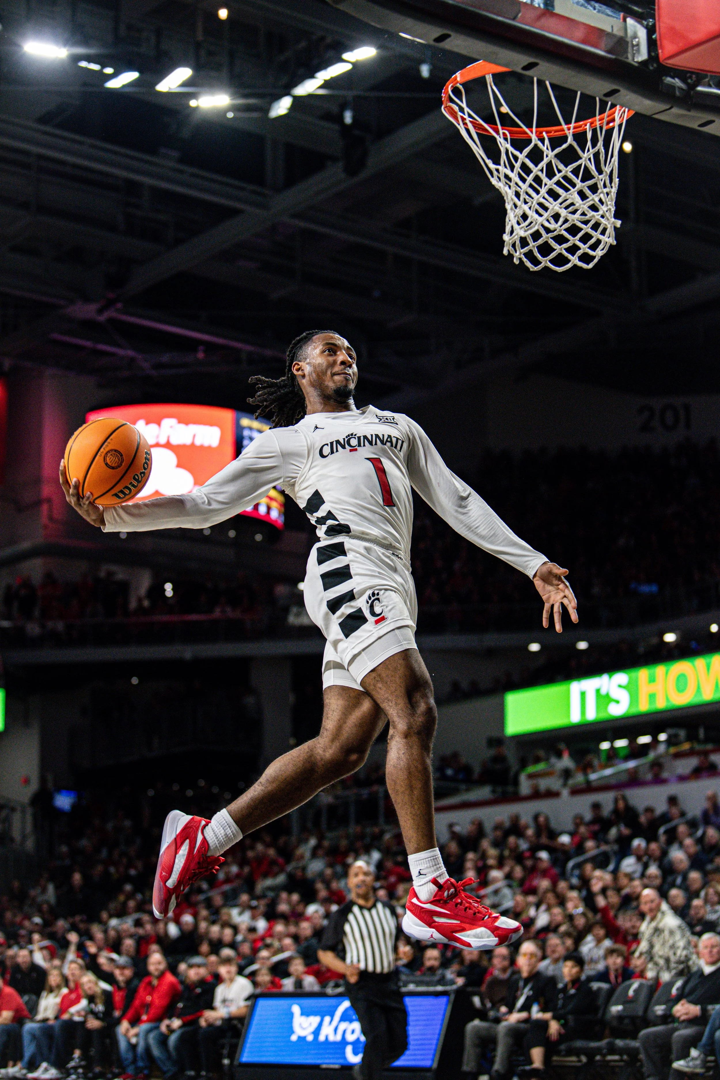 A basketball player from Cincinnati, wearing jersey number 1, is mid-air attempting a dunk during a game, with a crowd watching in the background.