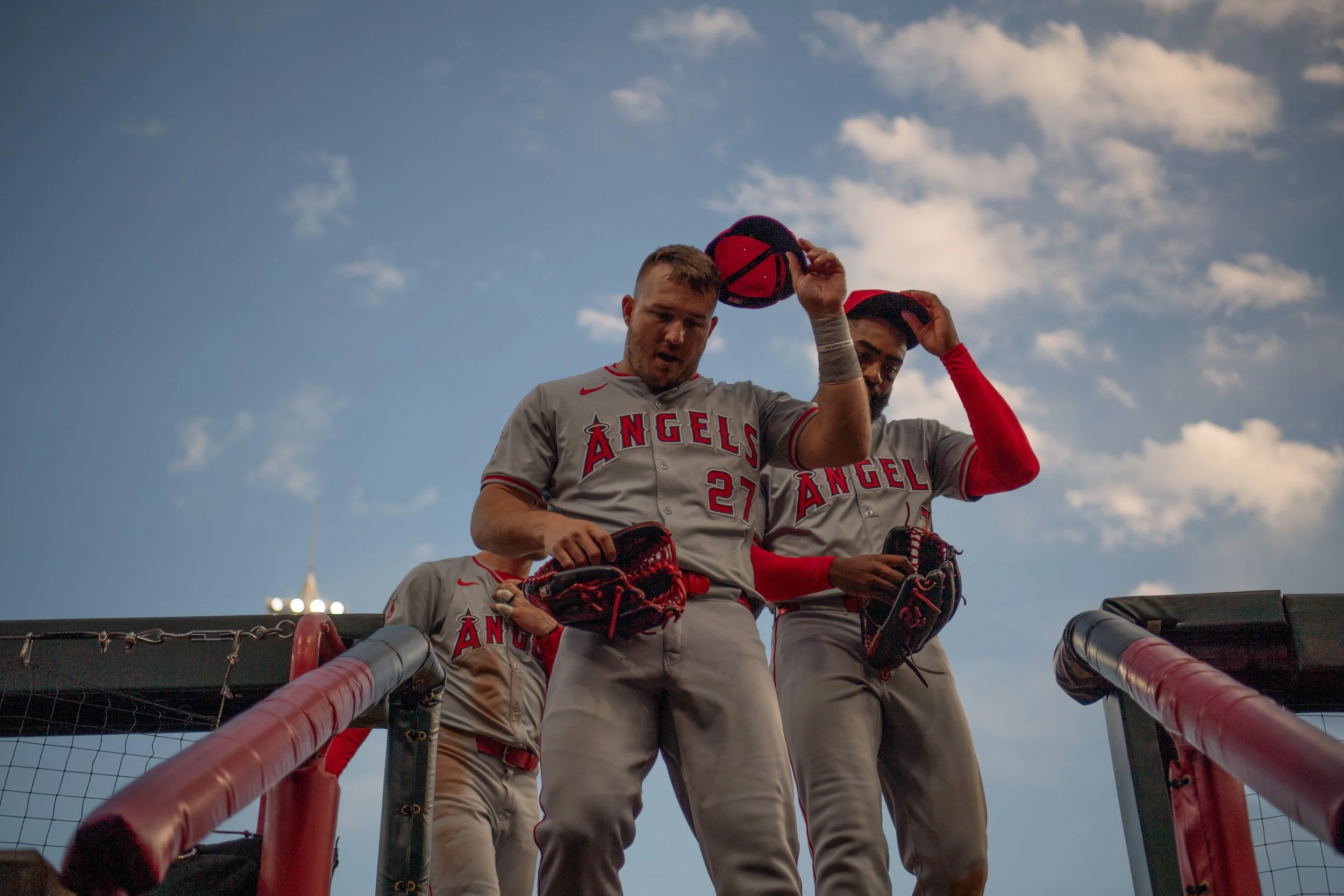 Baseball players from the Los Angeles Angels team standing on a dugout, looking down at the camera, with a blue sky and clouds in the background.