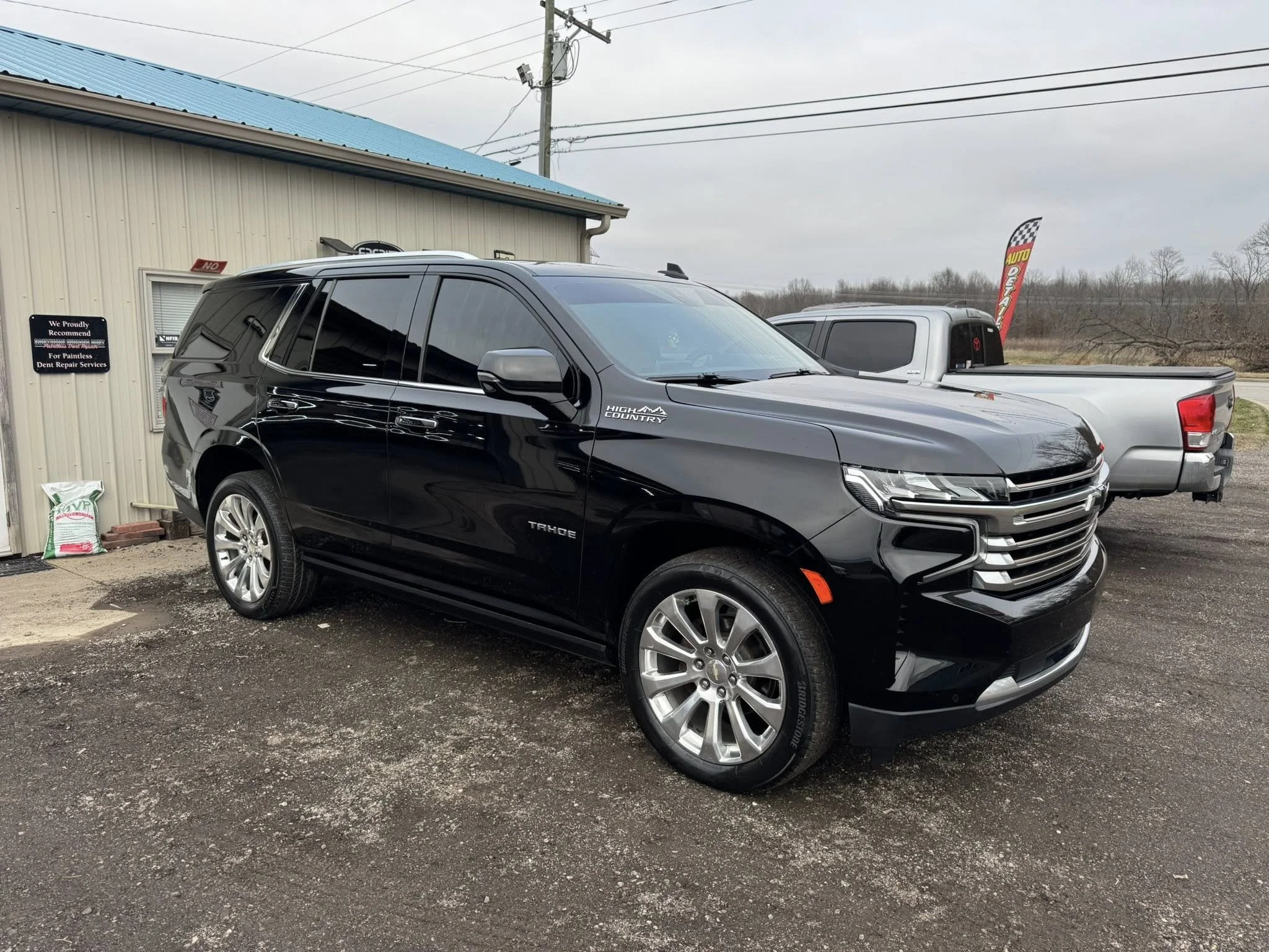 Black Chevrolet Equinox parked outside a building with a blue roof, alongside other vehicles, on an overcast day.