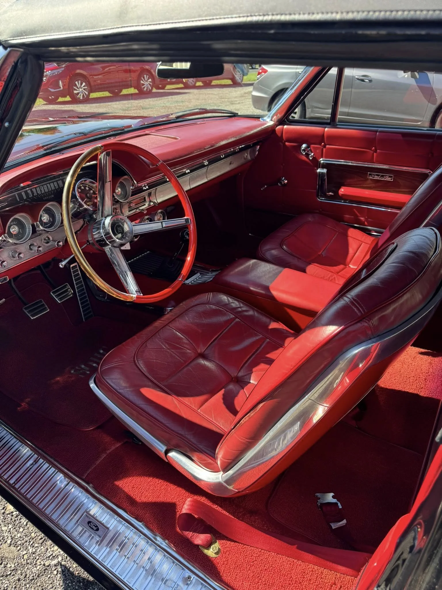 Interior of a vintage red car with red leather seats, a red dashboard, and a wooden steering wheel.
