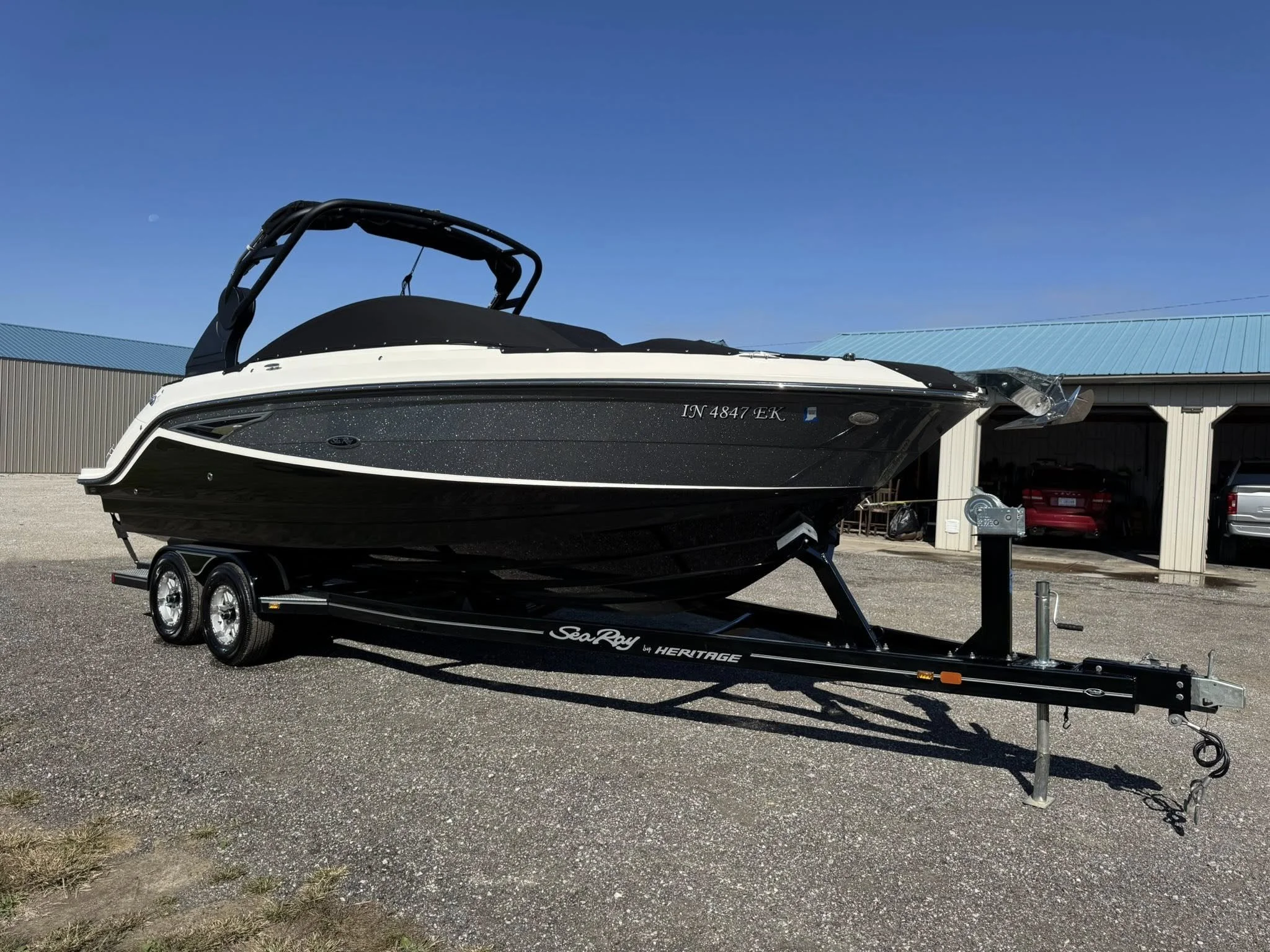 A black and white speedboat on a trailer in a gravel lot, with a large warehouse building in the background, under a clear blue sky.