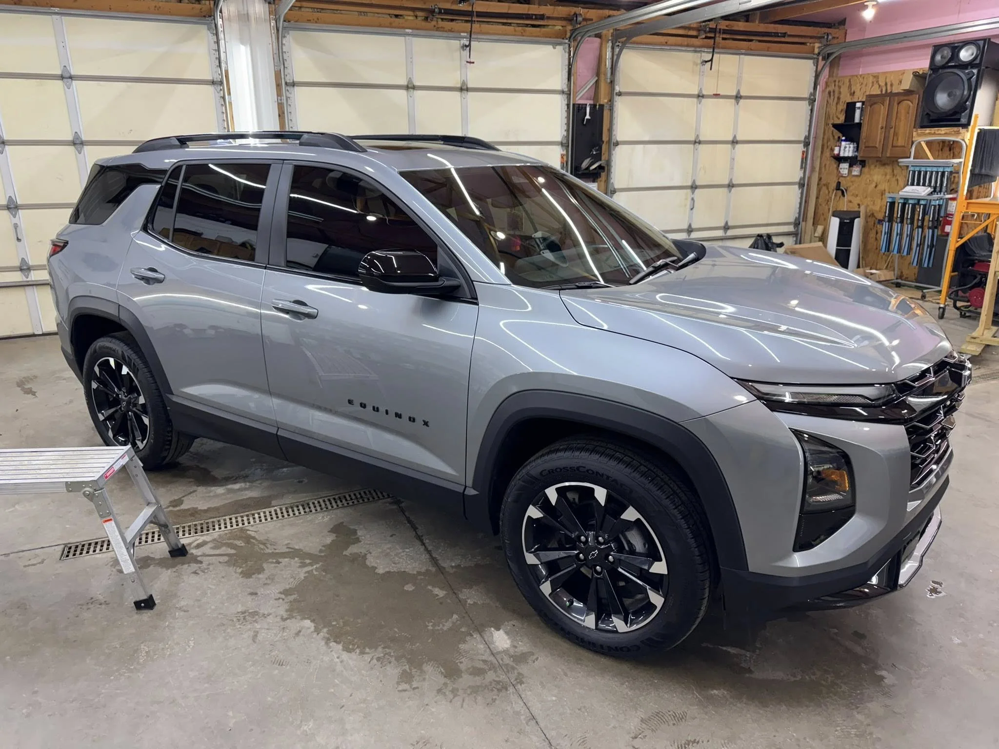 Silver Chevrolet Equinox SUV parked inside a garage with a concrete floor, garage door in background, and tools and equipment on shelves to the right.