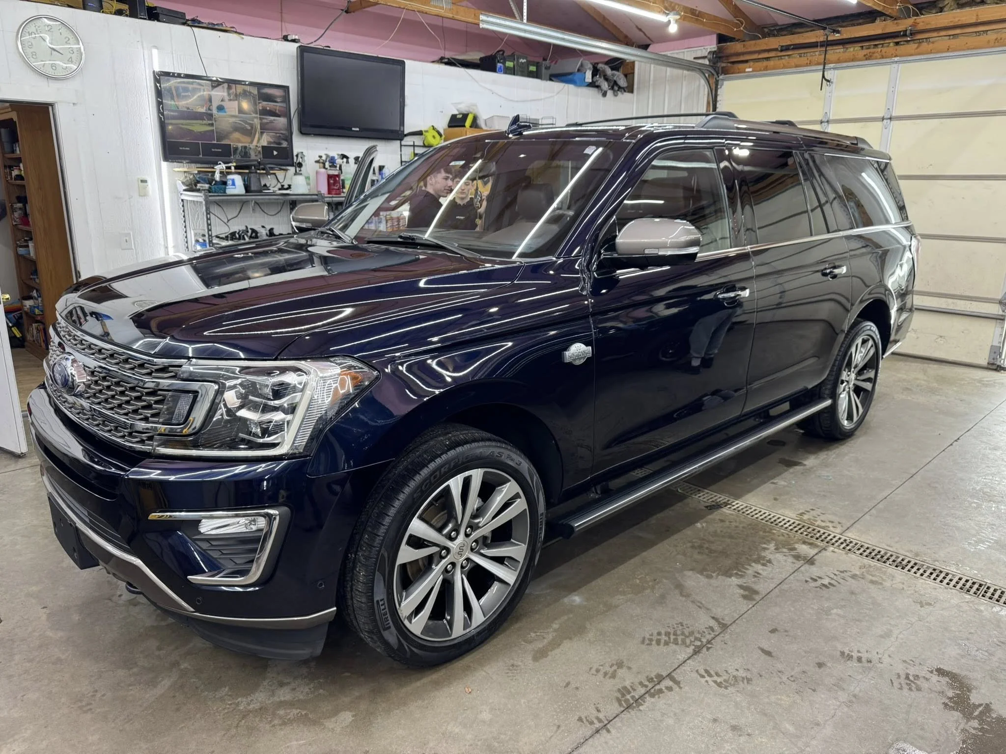 A black SUV parked inside a garage with tools and equipment on the shelves in the background.