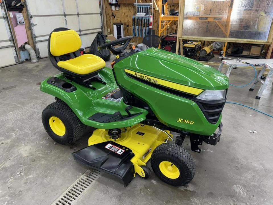 A green and yellow John Deere X350 riding lawn mower in a garage or workshop.