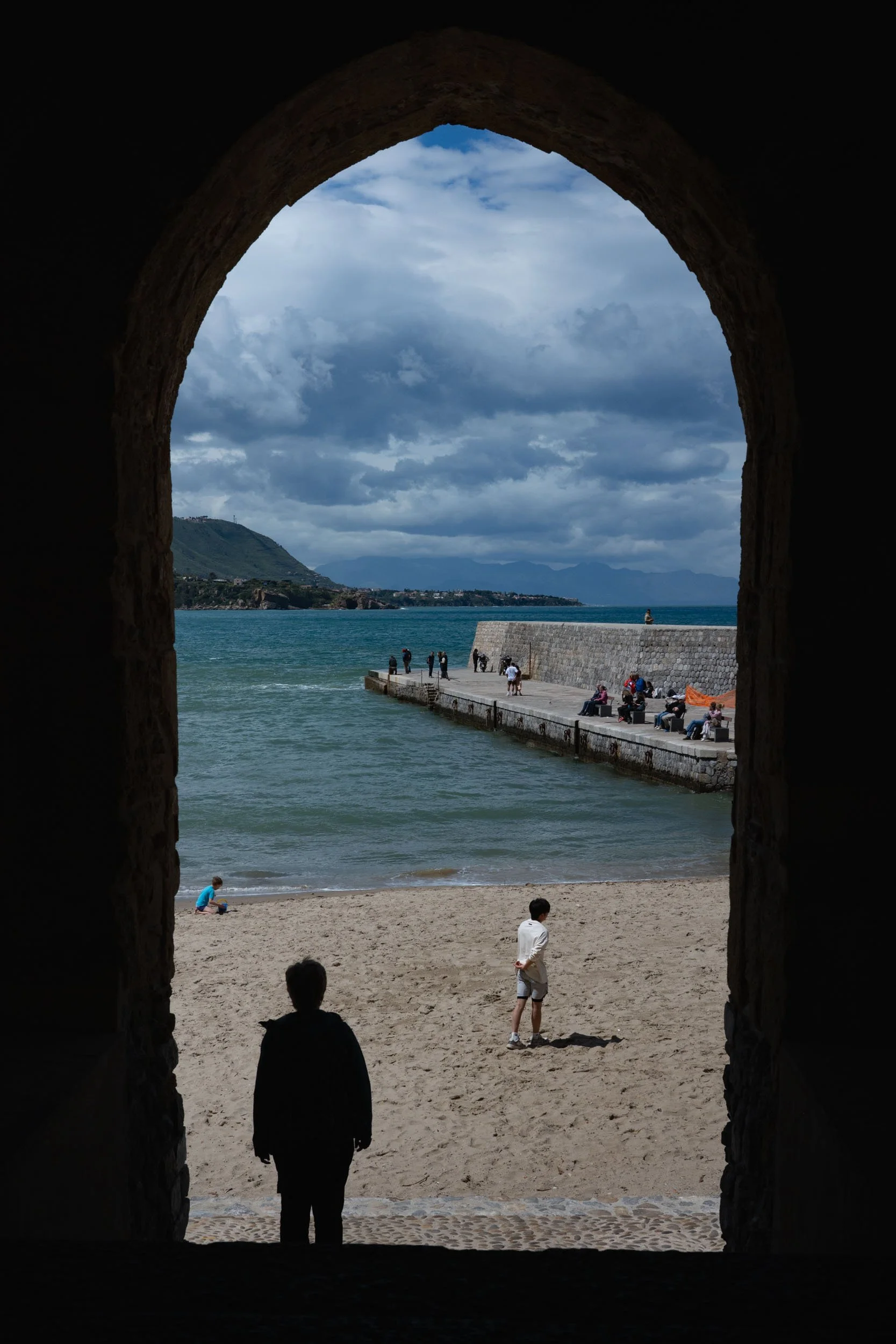 Colour photo taken in Sicily by Donna Lancia of through an archway with a boy in silhouette looking out at the sea beyond. 
