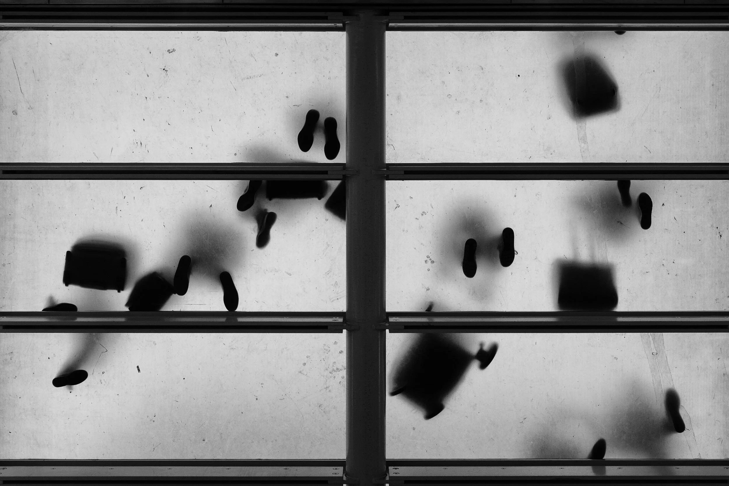 Black and white photos taken by Donna Lancia in London train station as seen from below.  Random travellers create an artistic and graphic image in silhouette. 