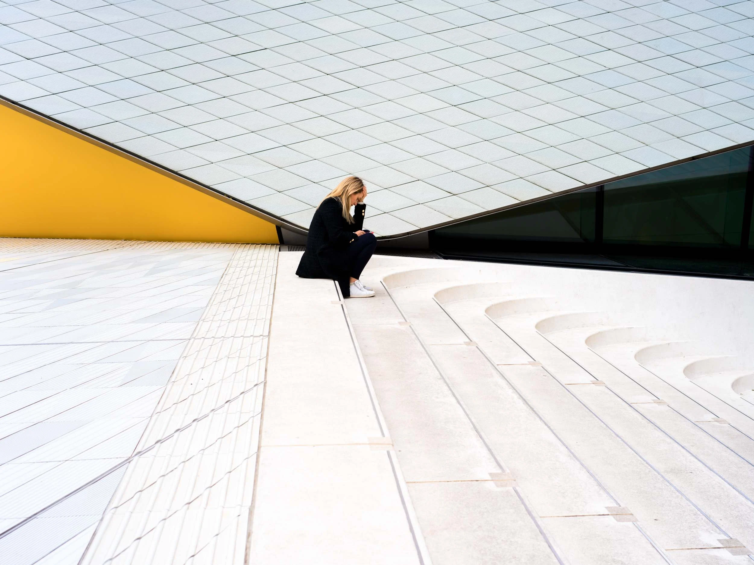 Color photo taken by Donna Lancia at a London museum of a woman seated in a graphically space where many  lines from the building and stairs intersect to form a graphical  composition. 