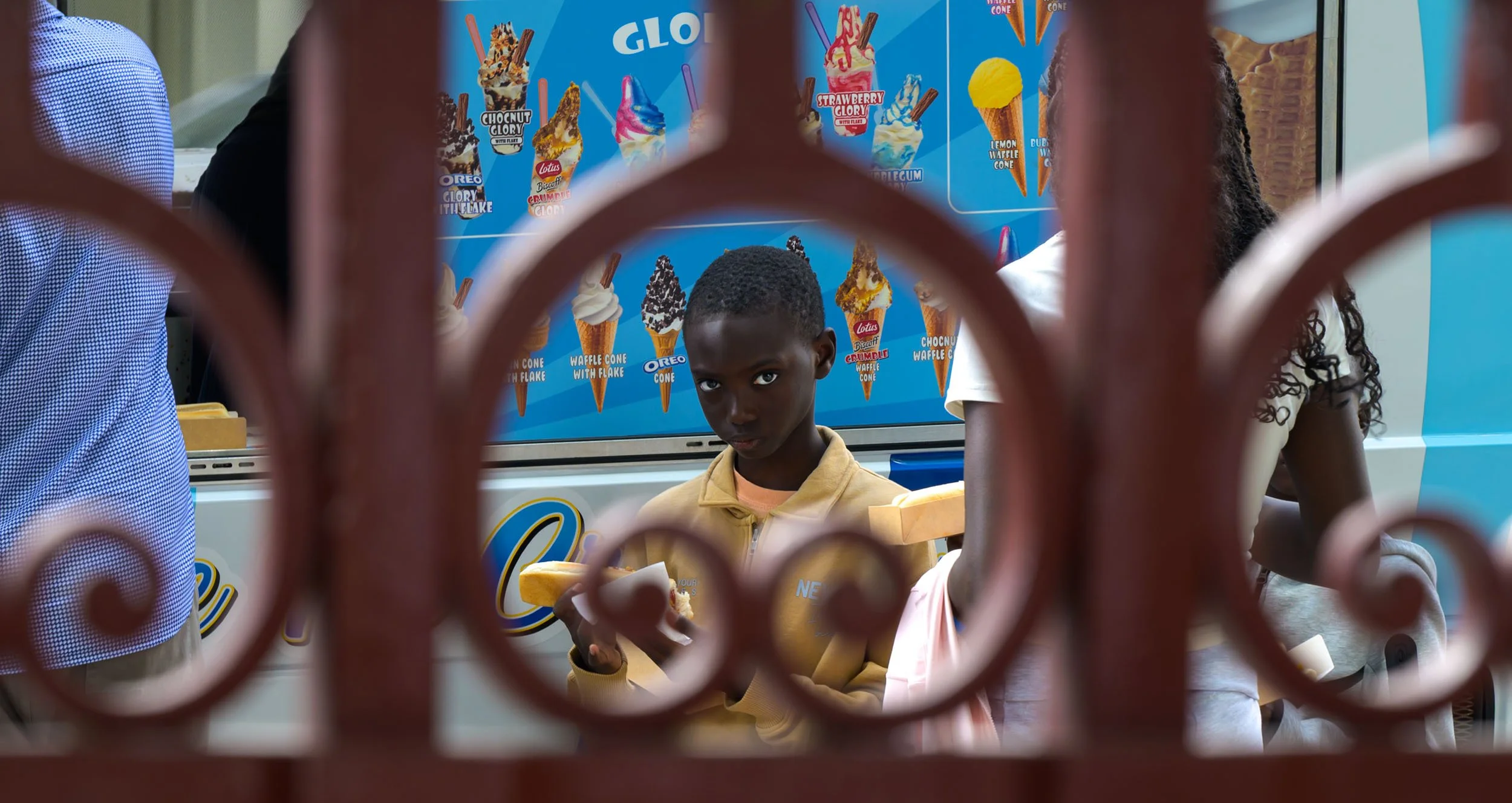 Colour photo taken by Donna Lancia in London of young boy through a railing with an engaging stare while eating his ice cream. 