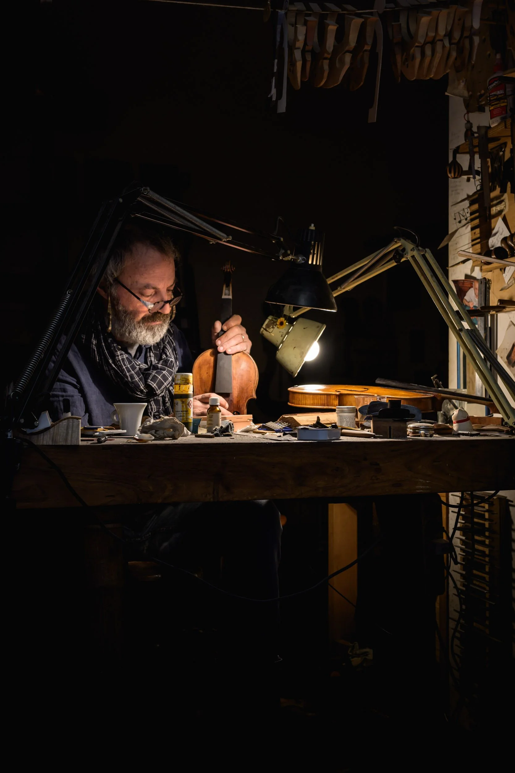 Color photo taken by Donna Lancia in Naples of a many making a violin by hand. The dark shadows and light is in the style of chiaroscuro.