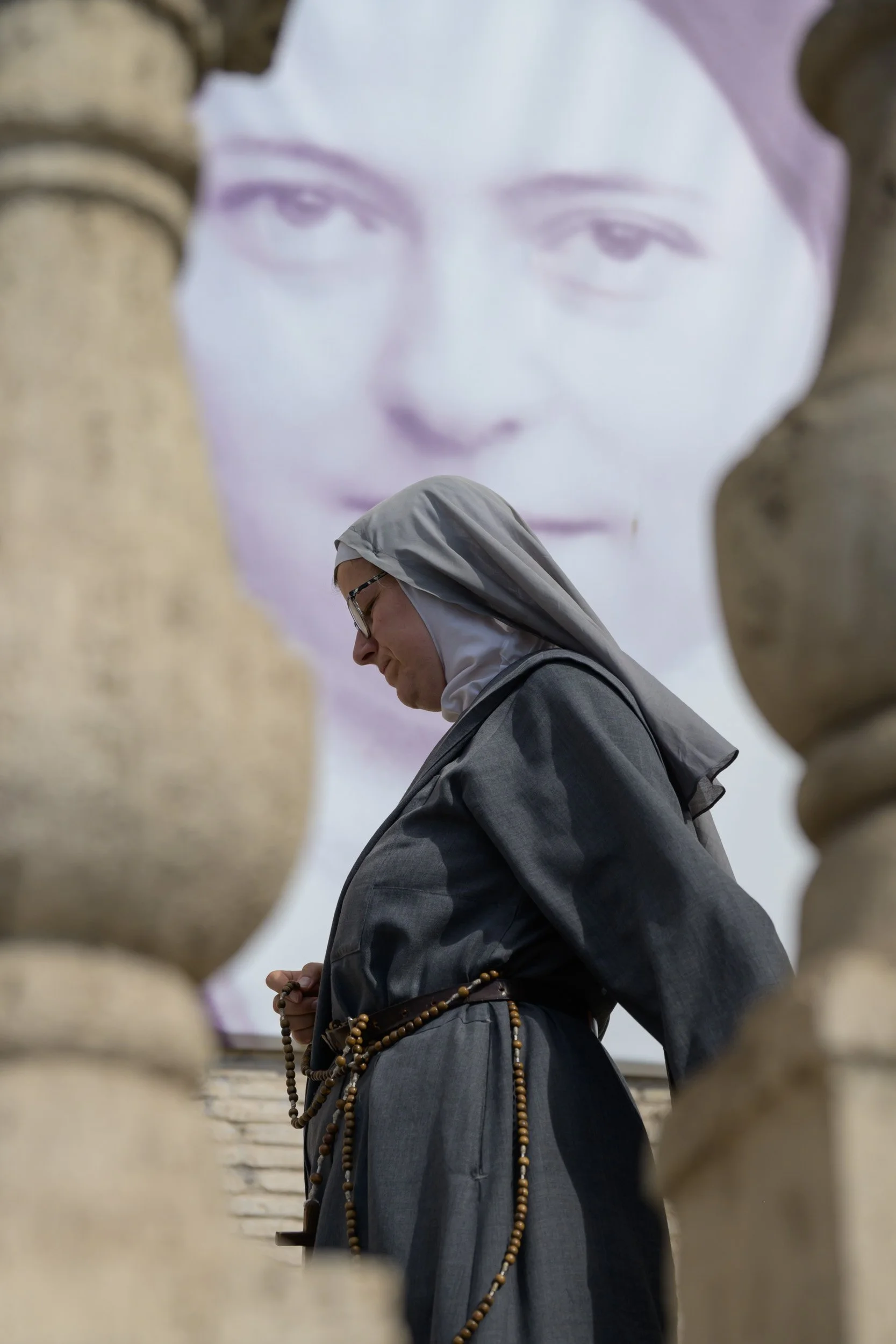 Color photo taken by Donna Lancia in Rome of a young nun framed by two stone railings of a church entrance with a photo of another nun behind.