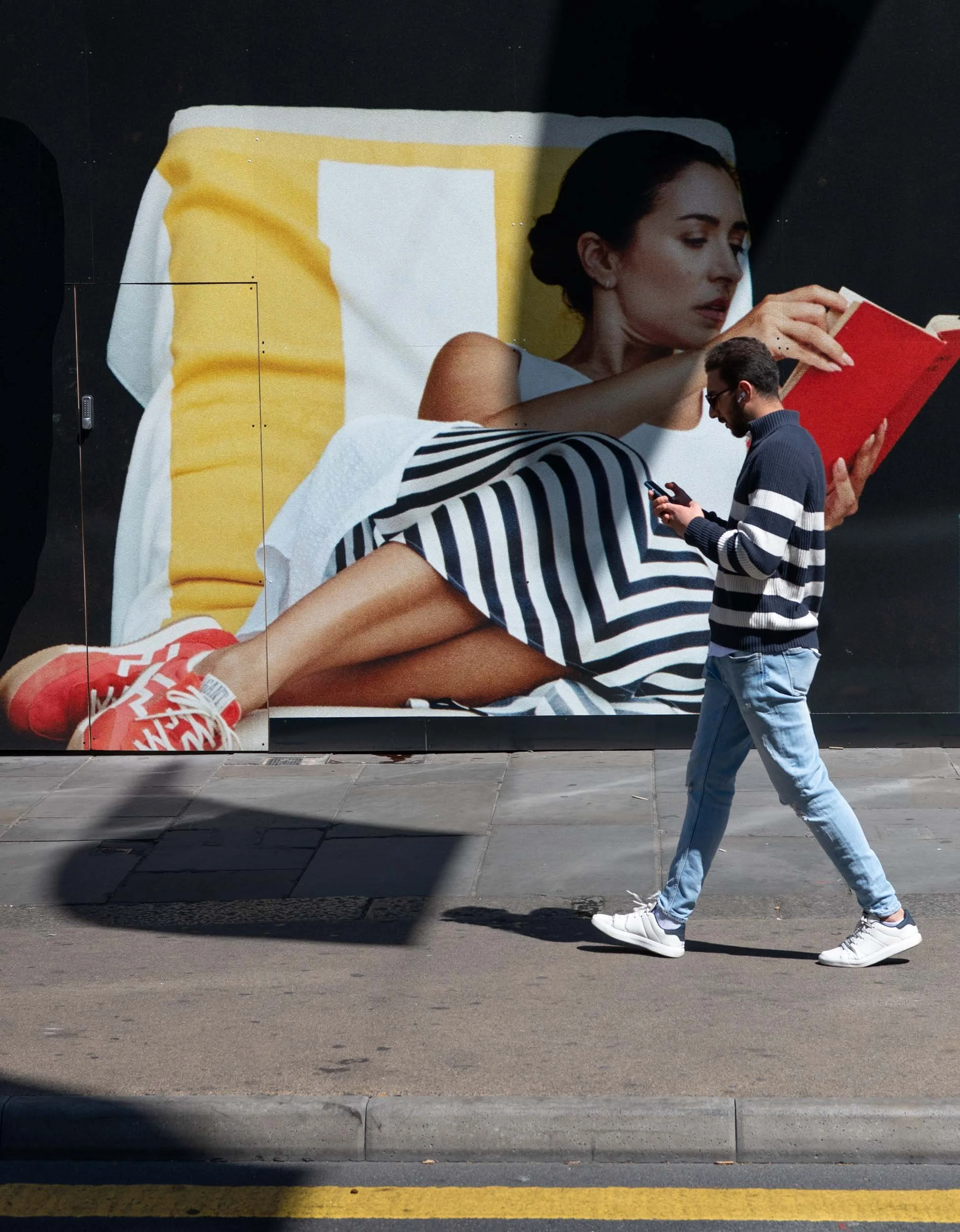 Colour photo taken by Donna Lancia in Venice of a man in a striped shirt that coincidentally matches the stripes in the woman's skirt in  billboard behind.  Titled reading between the lines. 