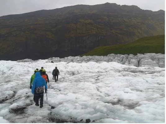Grupo de personas caminando sobre un glaciar con montaña de fondo.