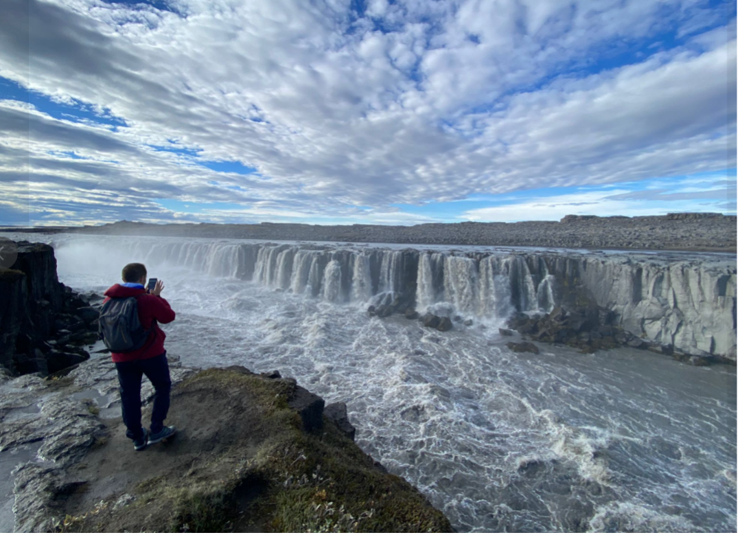 Persona con mochila tomando fotos cerca de las cataratas del río en un día nublado.