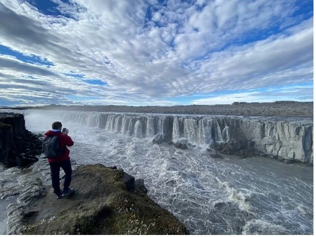 Persona tomando una foto de las cataratas del Iguazú en Argentina con un cielo parcialmente nublado.
