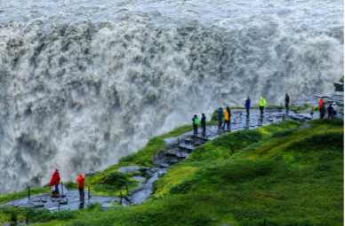 Personas observando una gran cascada desde un sendero con barandillas de seguridad.