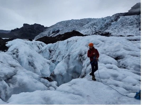 Esquimila con casco naranja, chaqueta roja y piolet en un glaciar de hielo y nieve