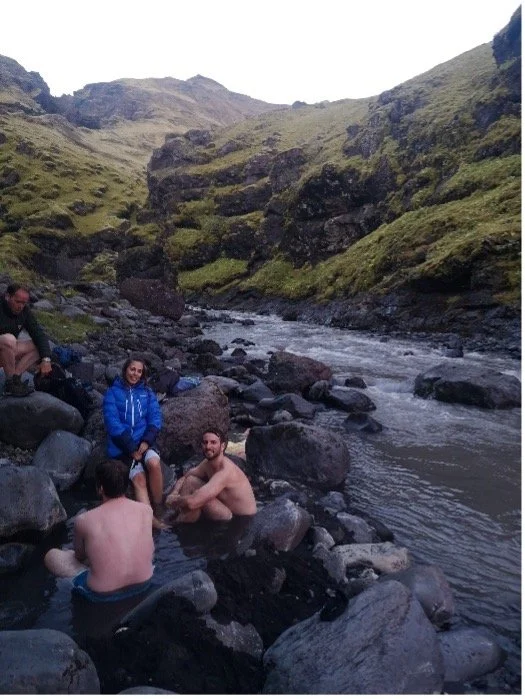 Cuatro personas en un río rodeadas de montañas verdes y rocas, disfrutando del paisaje y del agua.