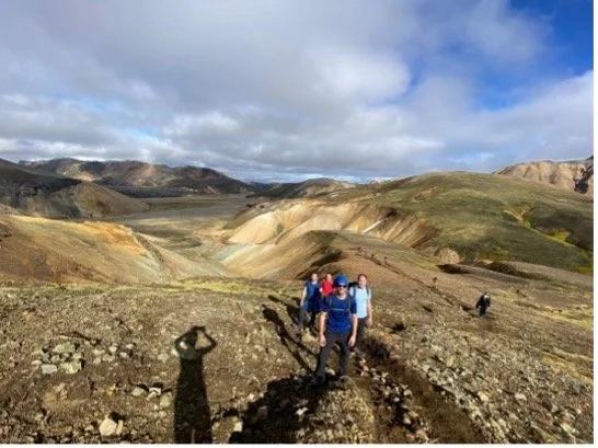 Grupo de personas caminando por un paisaje volcánico con colinas y cielo con nubes.