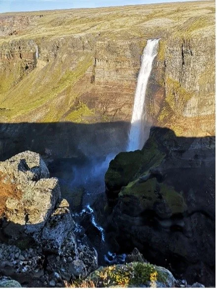 Cascada en un cañón con paredes de roca y vegetación, agua cayendo desde lo alto.