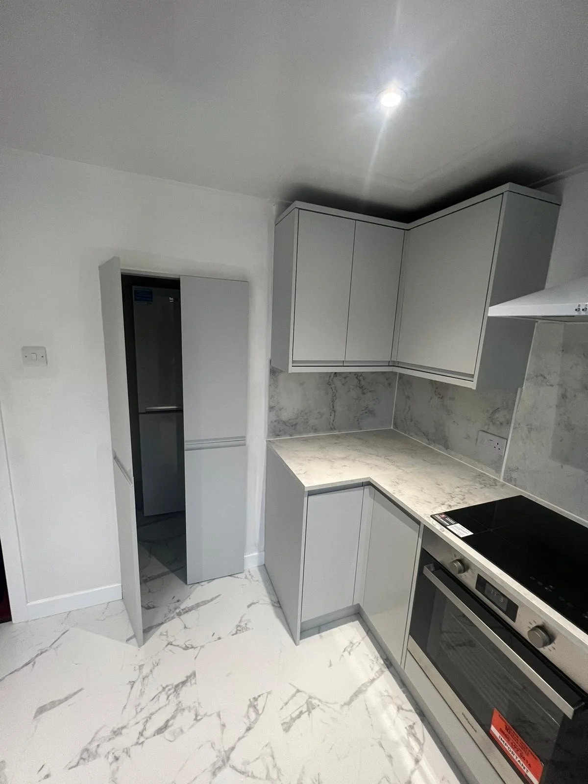 Modern kitchen with white cabinets, marble countertops, marble flooring, and an electric stove oven. There is a small open doorway leading to a room with a refrigerator.