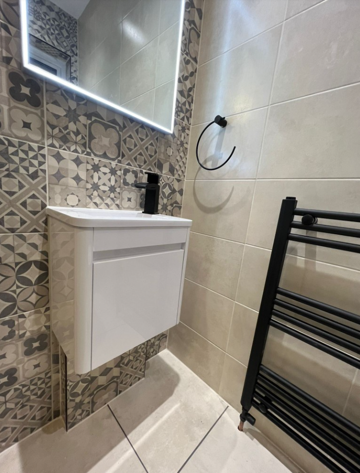 Modern bathroom with patterned tiles, a white wall-mounted vanity with a black faucet, a backlit mirror, a black towel ring, and a black heated towel rack.