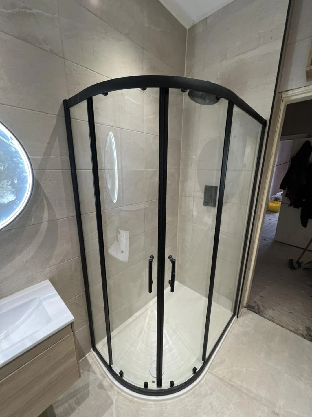 A corner shower with glass doors and black metal framing in a bathroom with beige tiled walls and floor.
