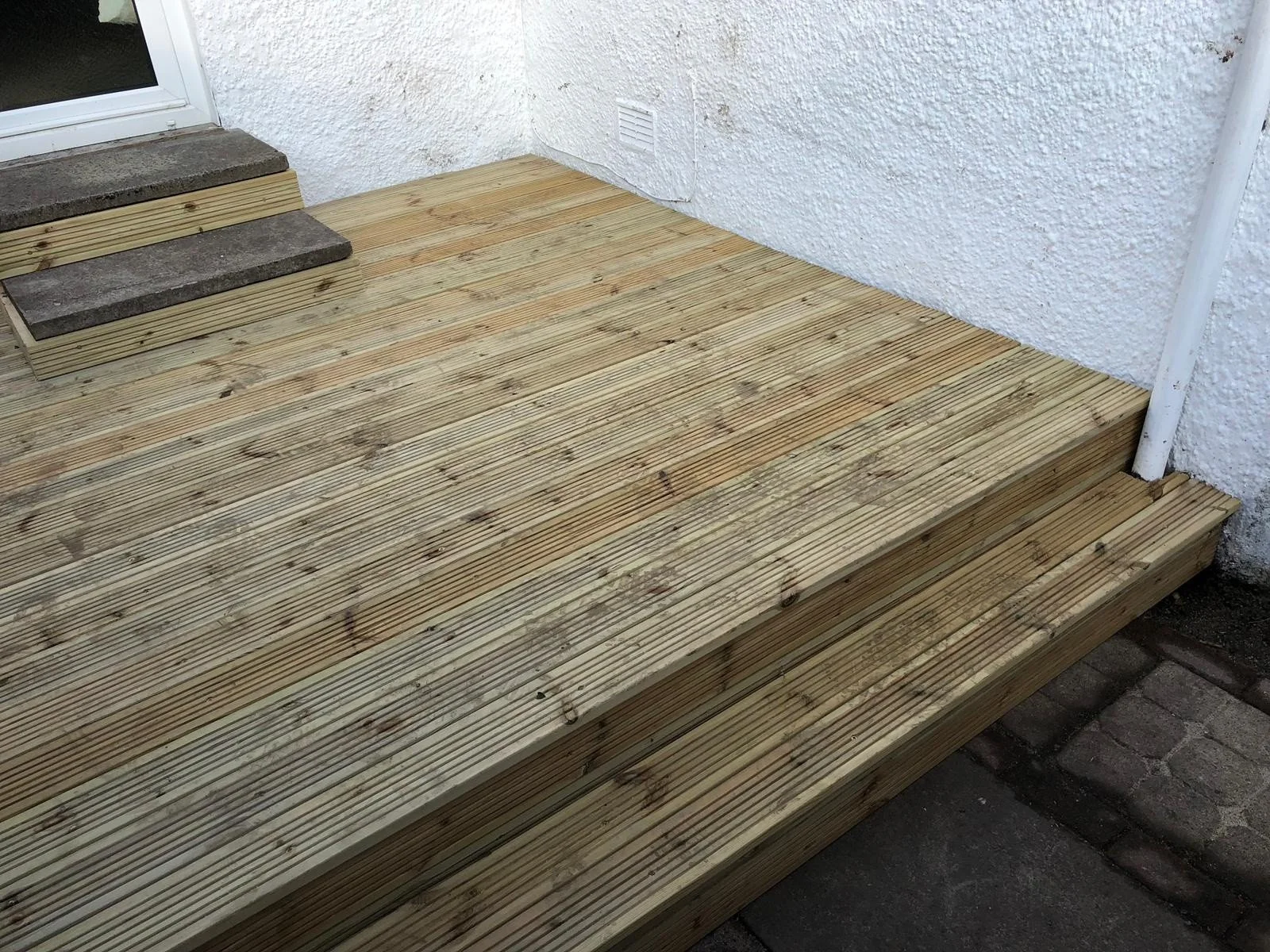 Newly built wooden deck with stairs next to a white wall and sliding glass door.