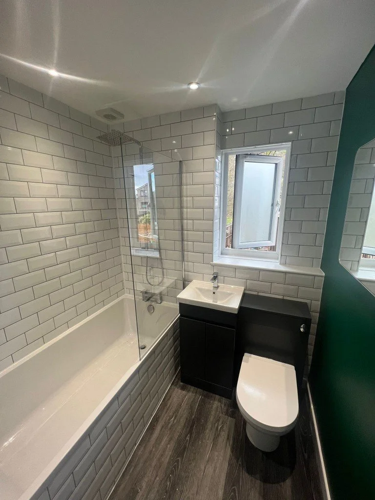 Small modern bathroom with white subway tiles, black vanity with a small sink, a toilet, and a window letting in natural light.