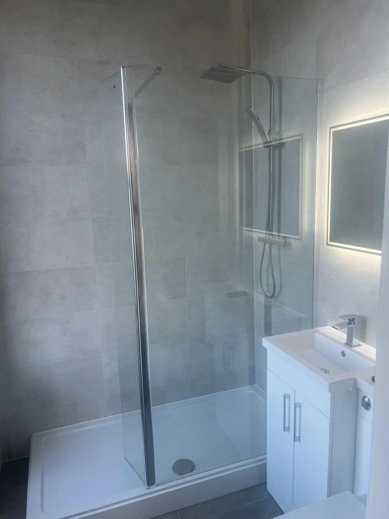 A modern bathroom with a glass-enclosed shower, a shower head, and a small white sink with a mirror above it.