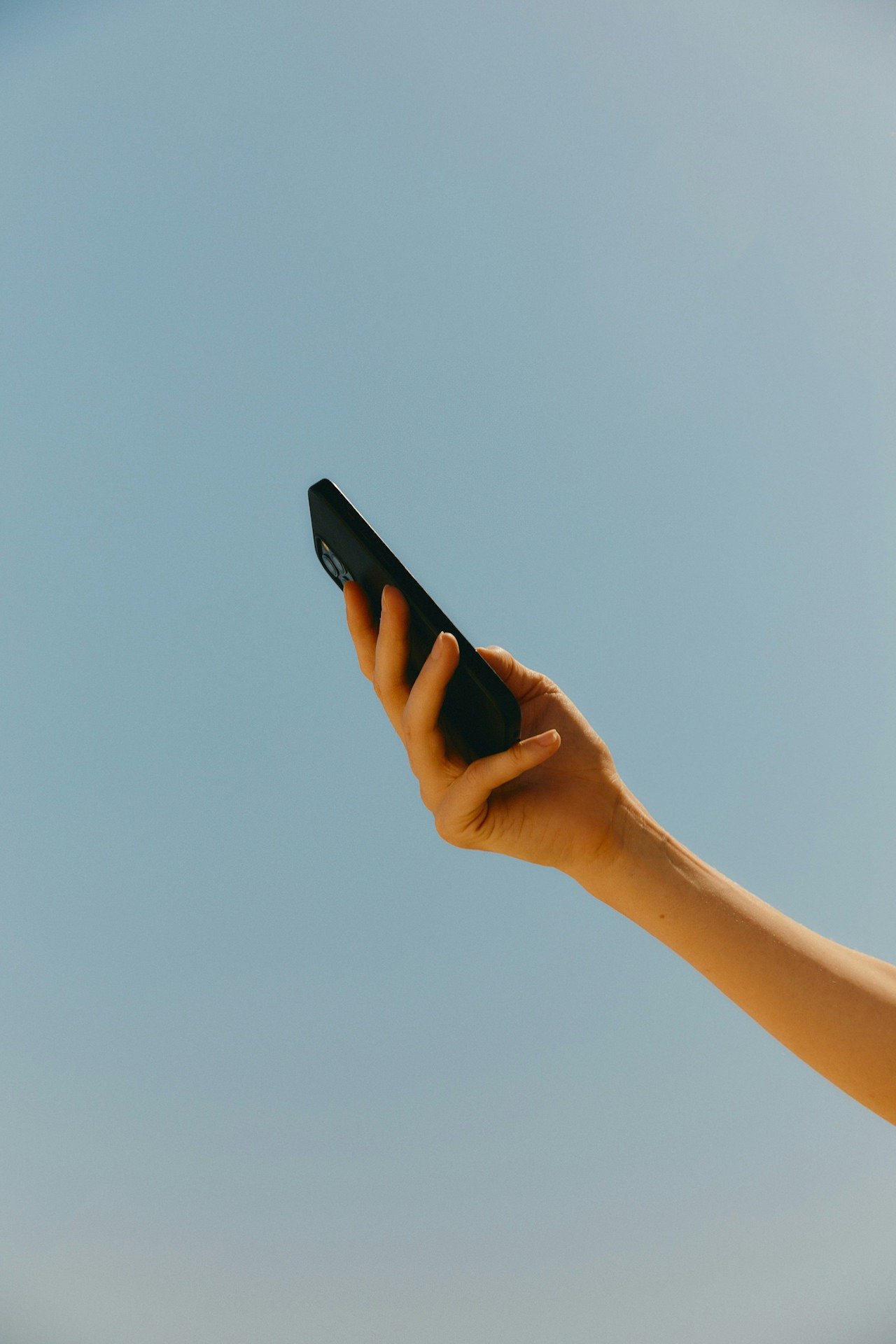 Person's hand holding a mobile phone up in the air in front of a blue sky