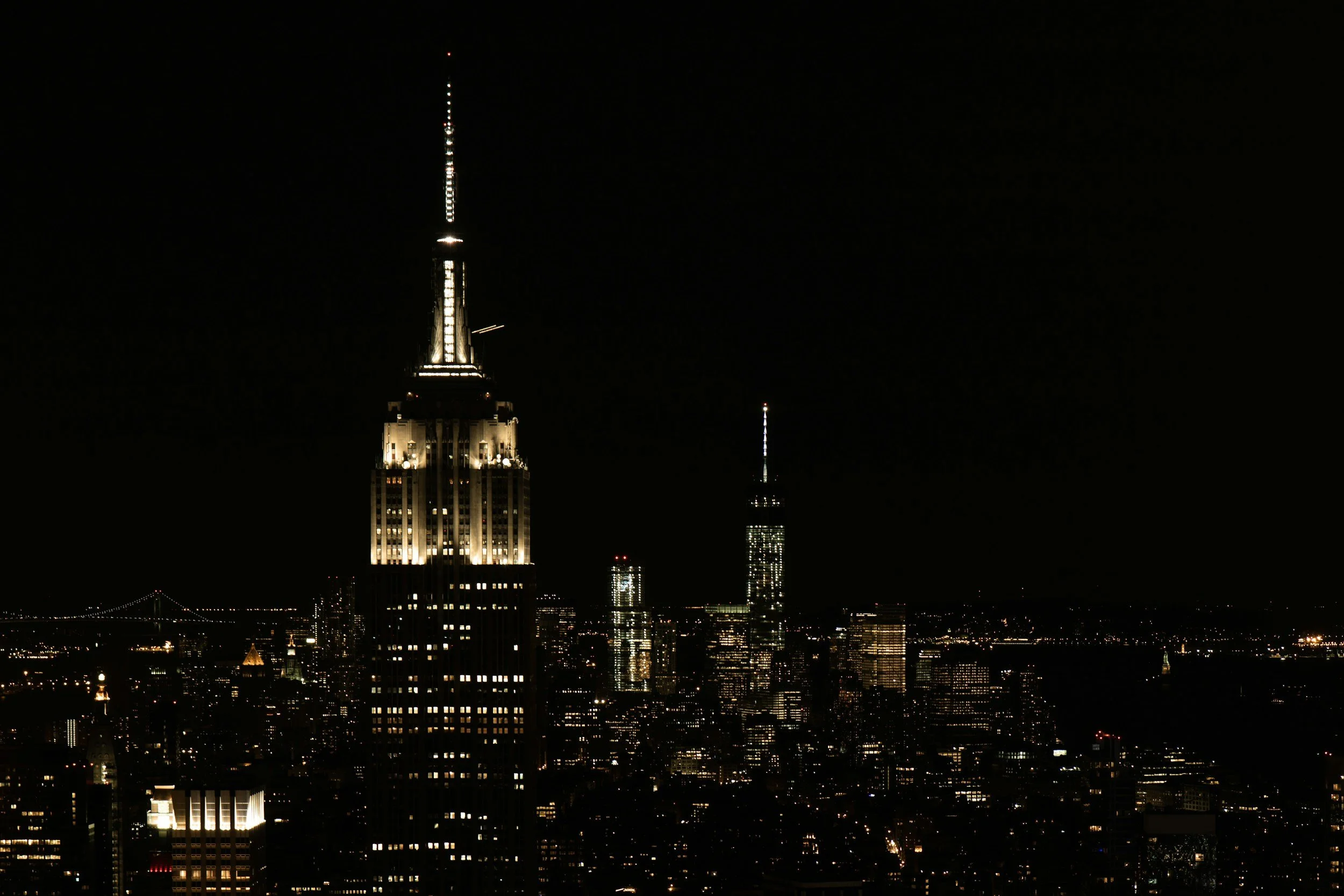 View of the New York City skyline with skyscrapers and the Brooklyn Bridge over the East River on a cloudy day.