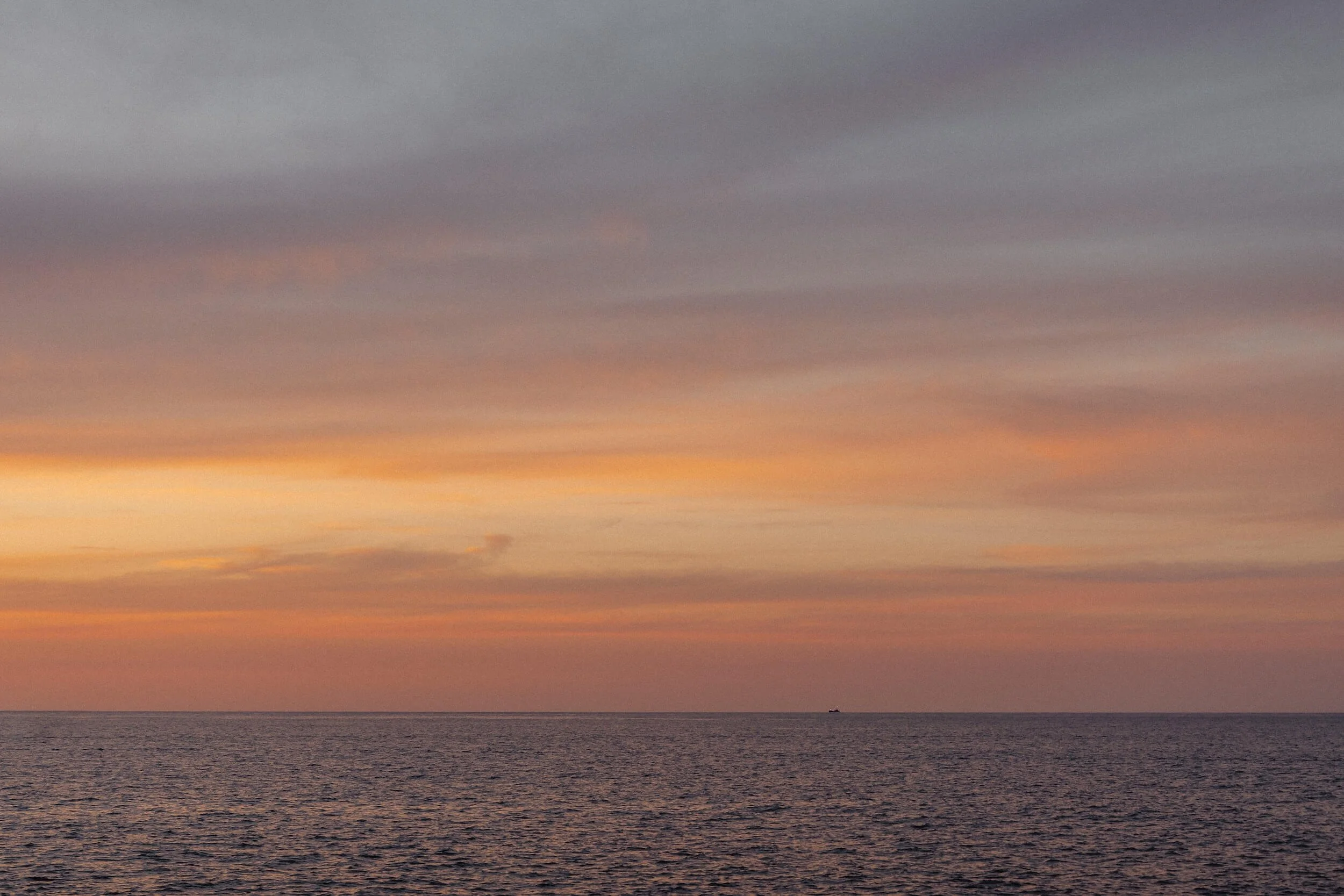 A sunset over the ocean with a colorful sky of pink, orange, purple, and gray clouds.