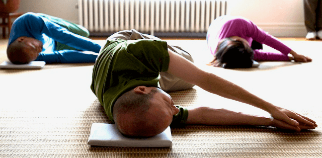 People practicing Feldenkrais Awareness Through Movement®, kneeling on mats with arms extended forward.