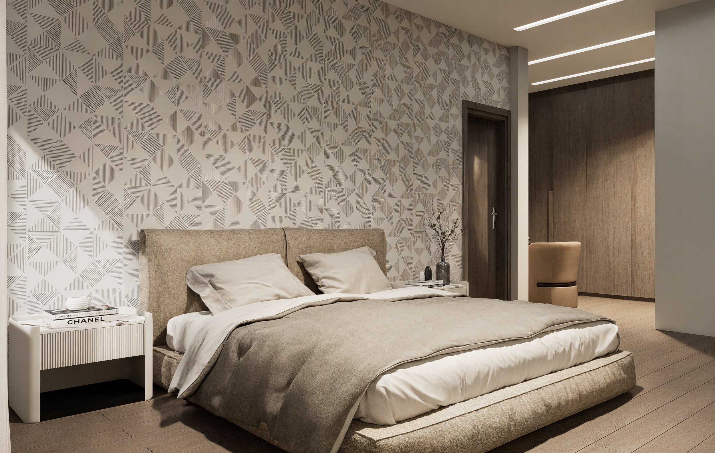 Modern bedroom with beige upholstered bed, beige linens, patterned wall behind the bed, white bedside table with books, vase with branches, and a beige chair in the corner.