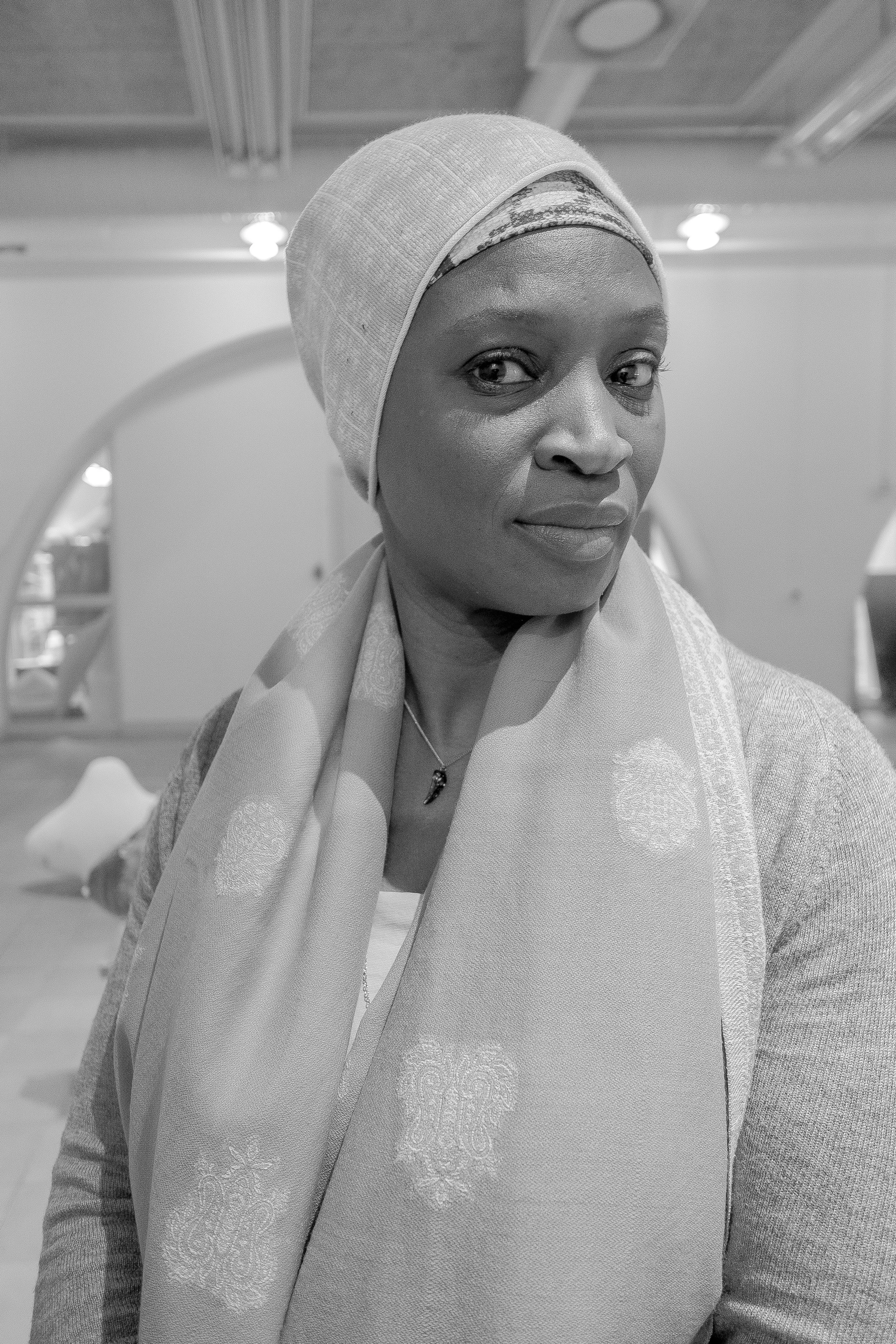 Marcia Kure wearing a headscarf and a textured shawl looks directly at the camera in a well-lit indoor setting.