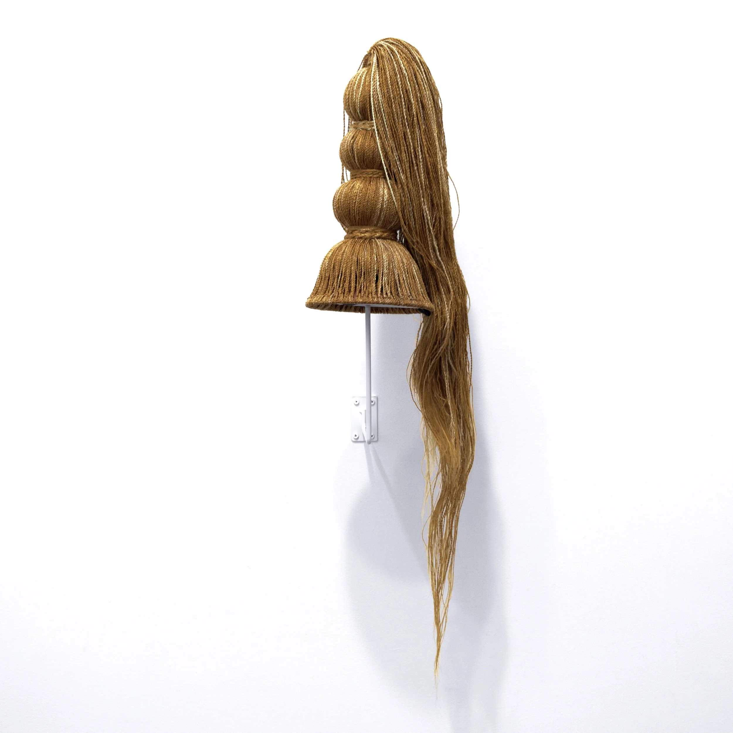 Wall-mounted sculptural headdress resembling a hairstyle with multiple buns and cascading braided synthetic hair.