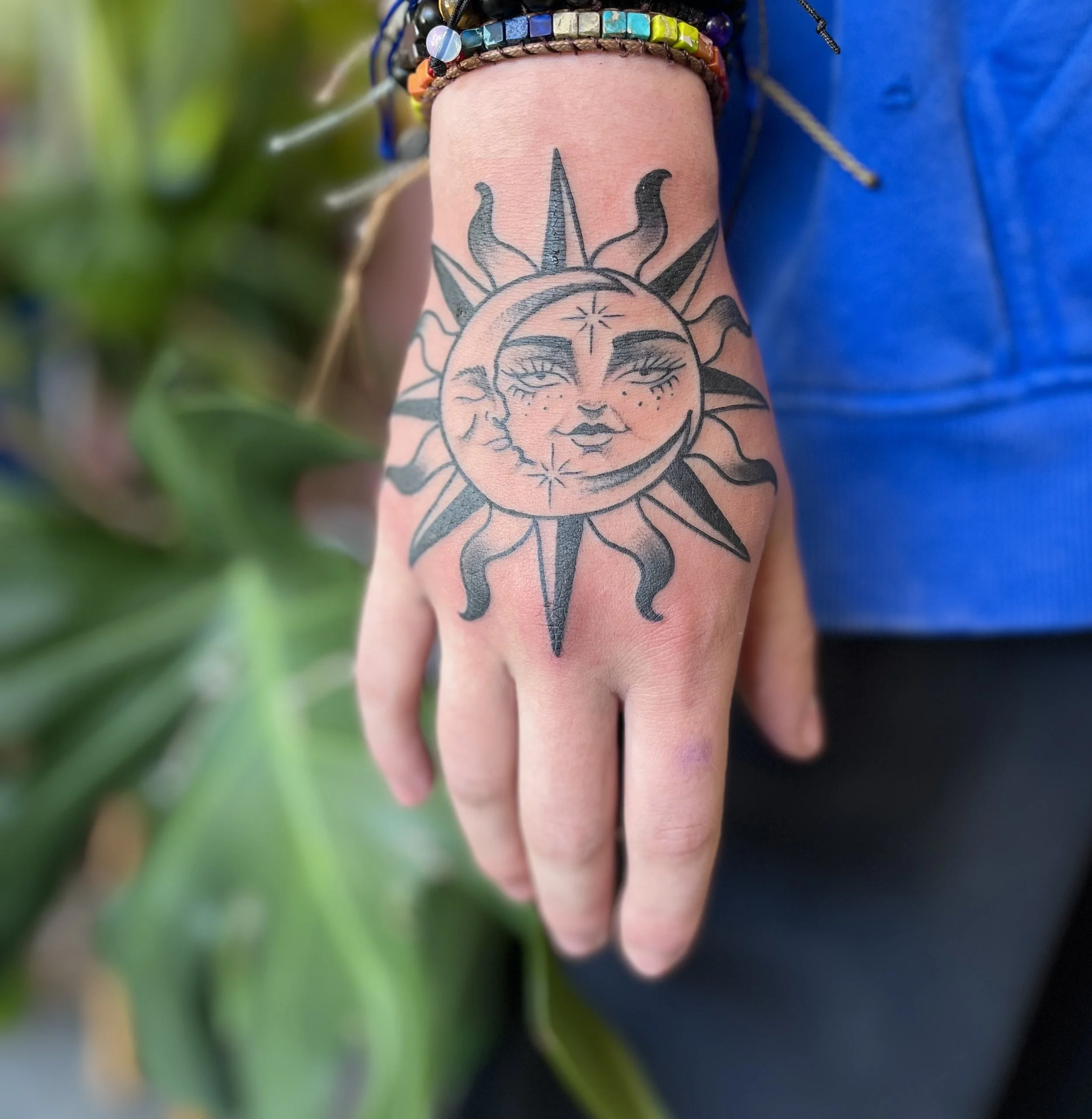 Tattoo of a sun and moon with a woman's face, on a person's hand.