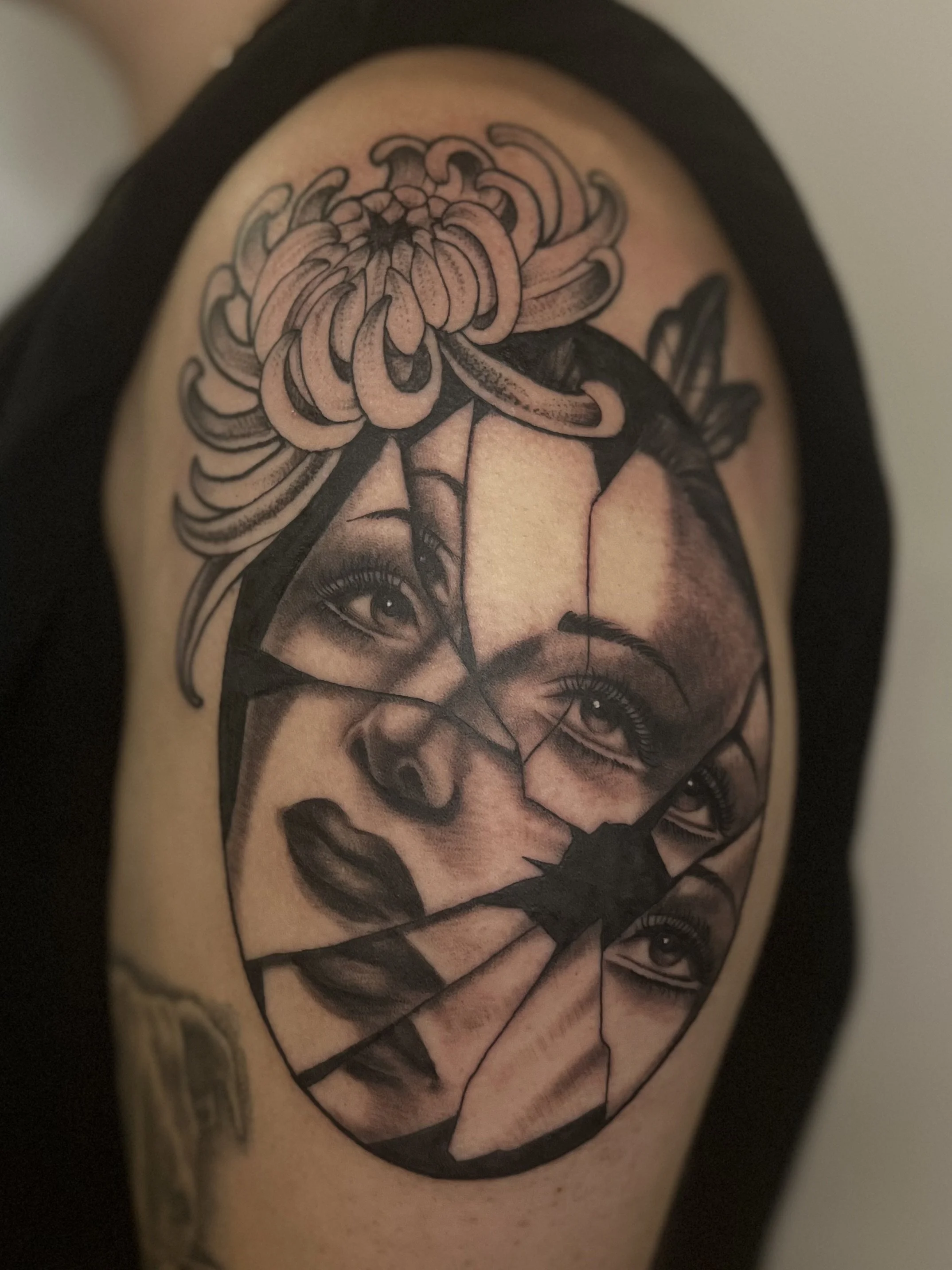 Black and gray tattoo of a woman's face with layered and fractured sections, featuring detailed eyes and lips, topped with a large, detailed flower.
