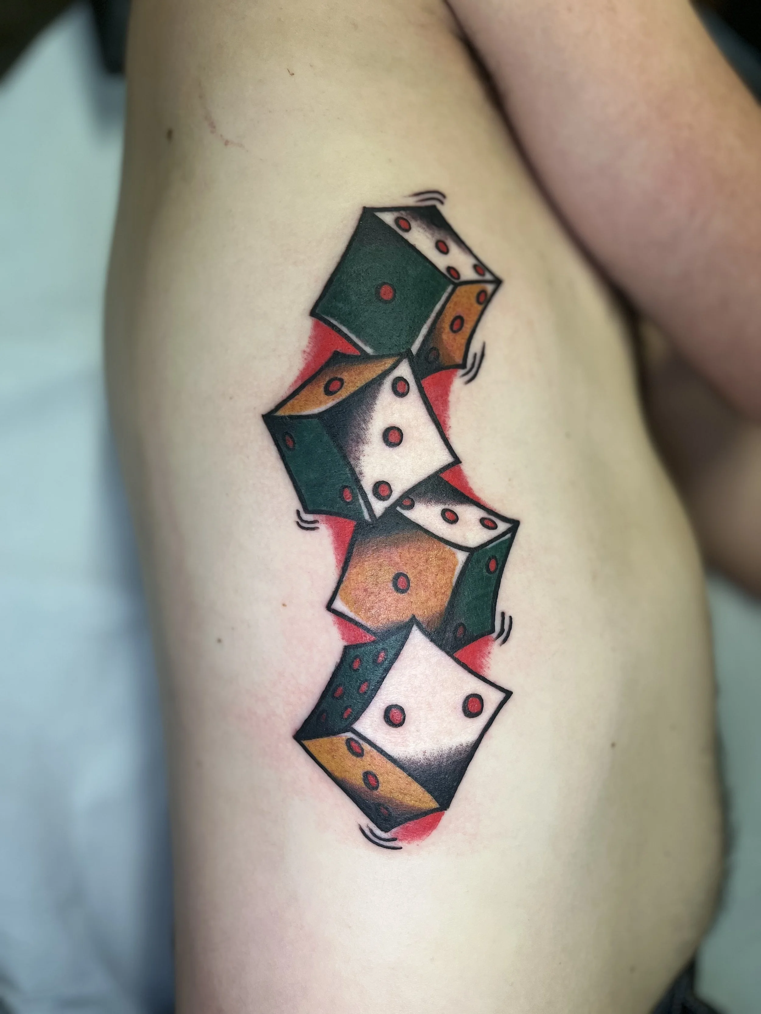 American traditional ribcage tattoo of five dice in various colors, surrounded by red shading.