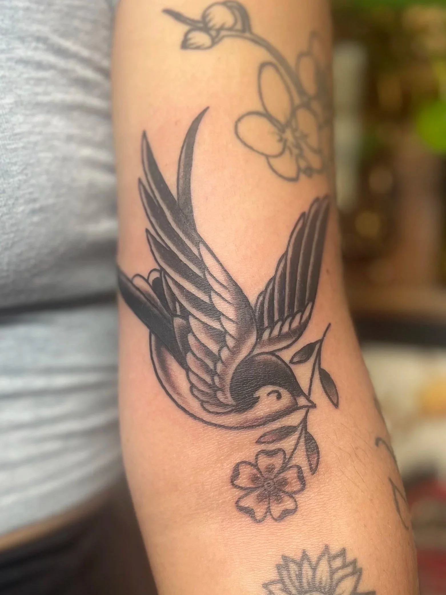 Tattoo of a swallow carrying a flower in its beak on a person's arm.
