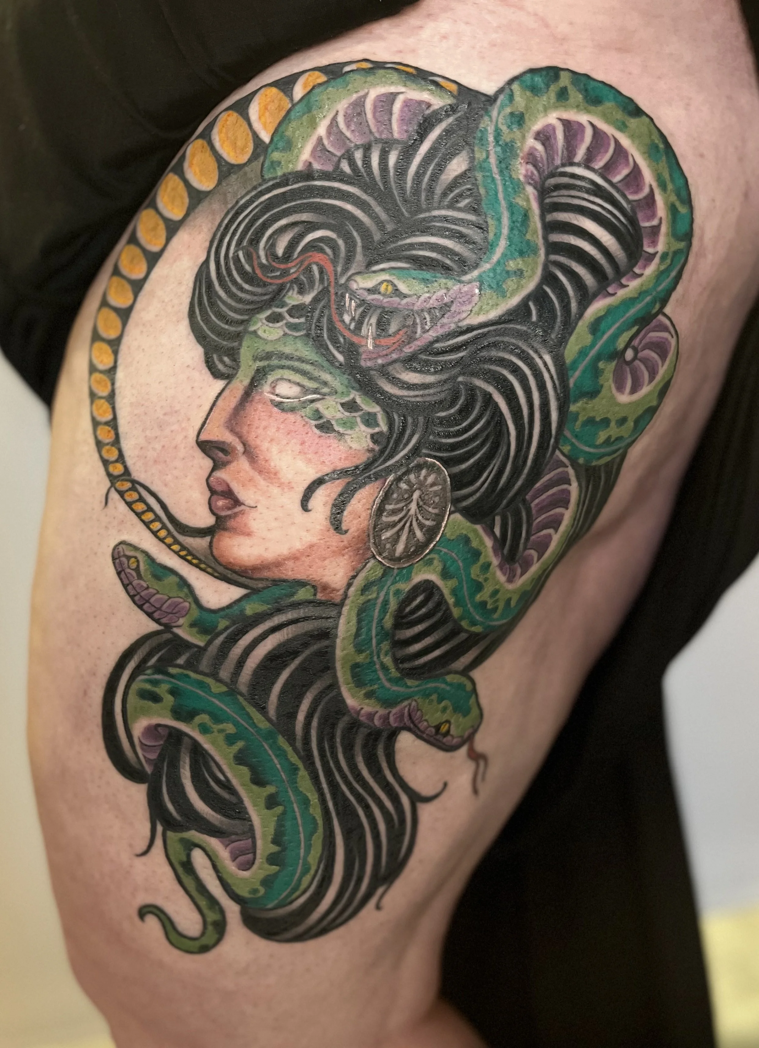 Tattoo of a woman's face with black hair intertwined with a snake and a snake's head emerging near her head, with colorful accents and details.