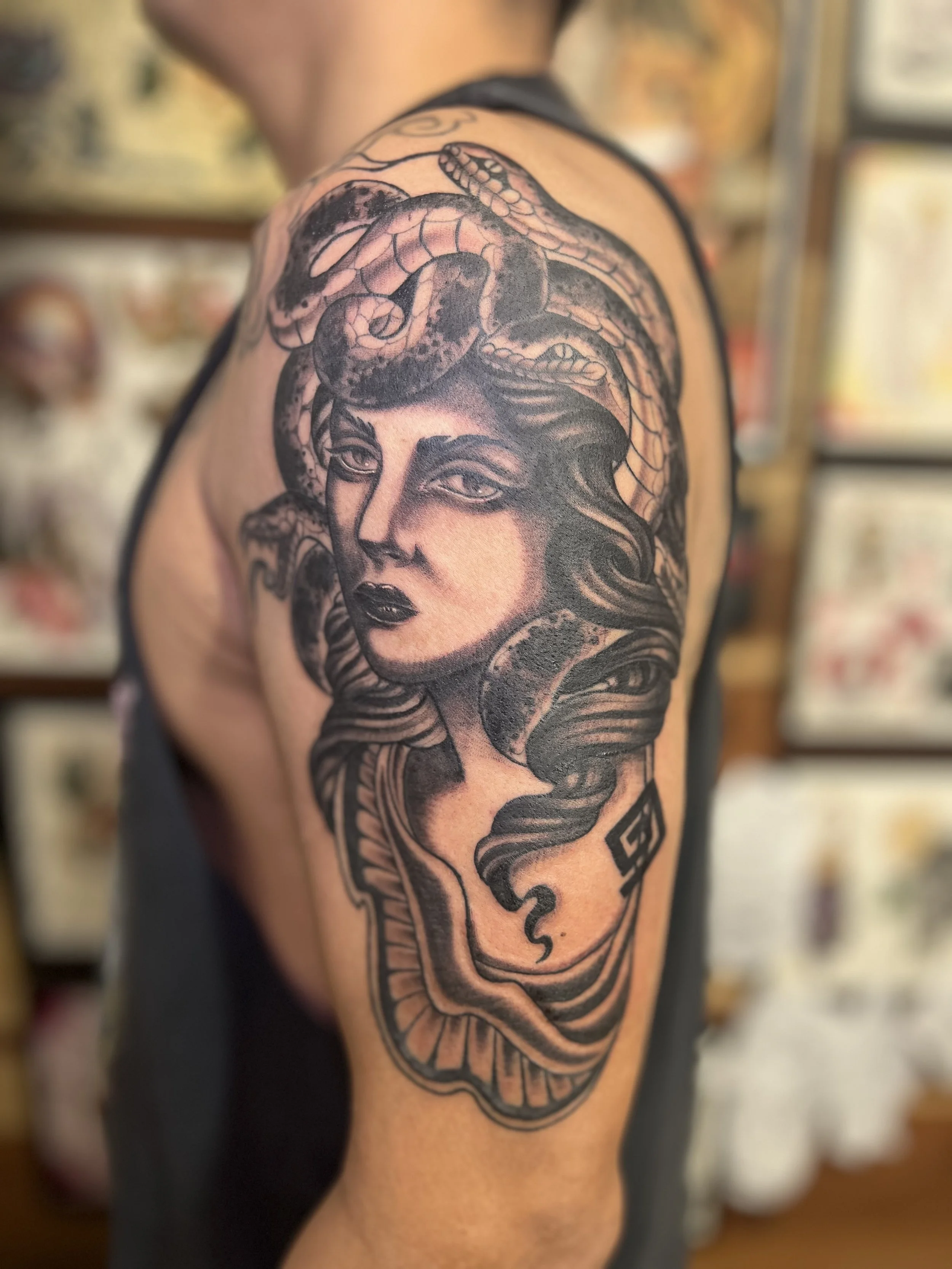 Black and gray tattoo of Medusa with snake hair on man's shoulder.