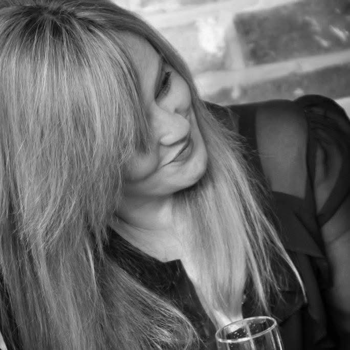 Emma Macleod smiling and looking down, holding a glass, in black and white.