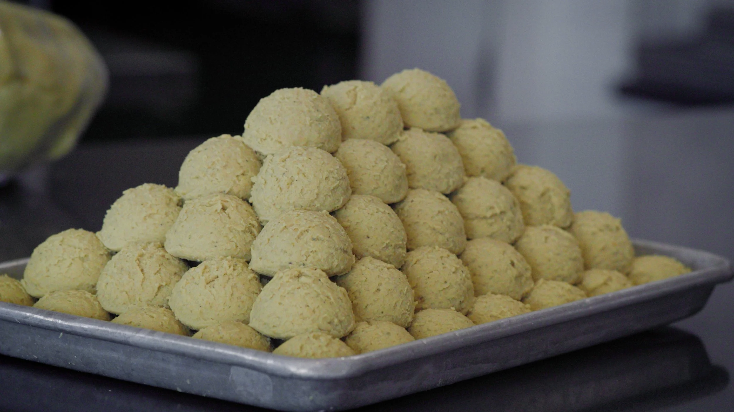 A tray of raw, pale yellow balls of masa arranged in a pyramid shape.