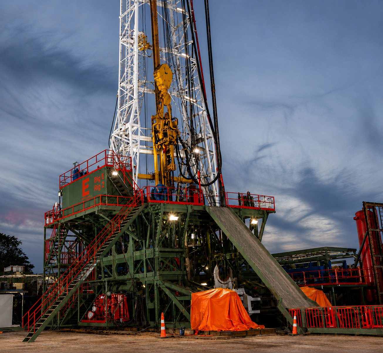 An oil drilling rig with a tall white tower, yellow machinery, and red safety railings on a cloudy evening.