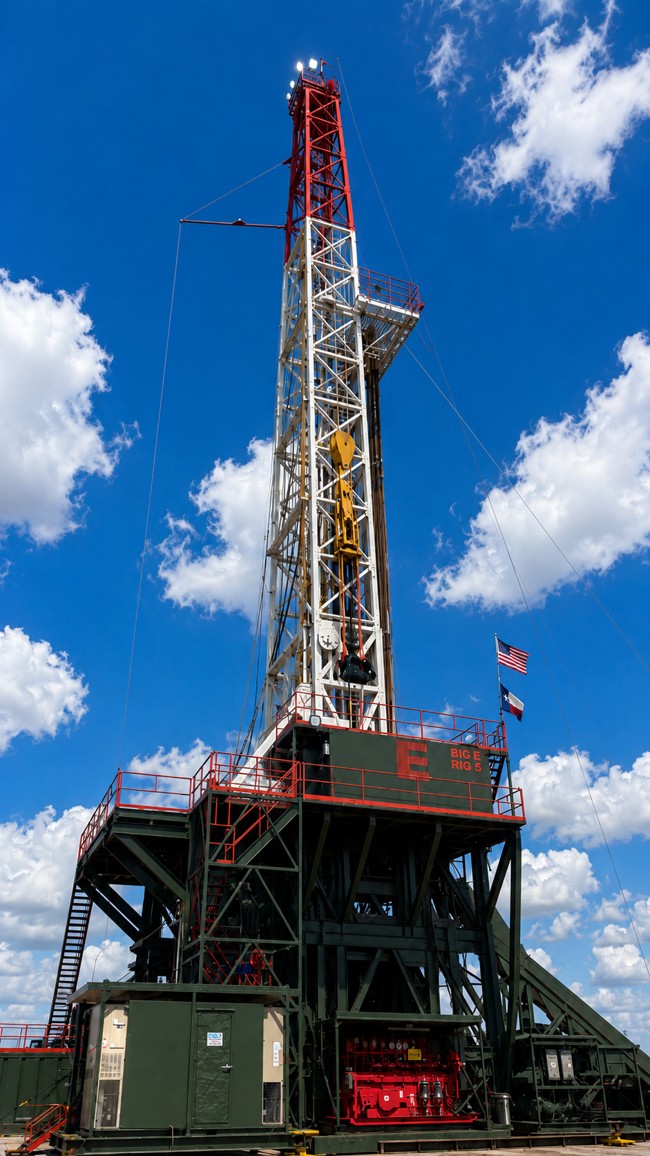 An offshore oil drilling rig with a tall derrick against a bright blue sky with scattered clouds and an American flag flying.