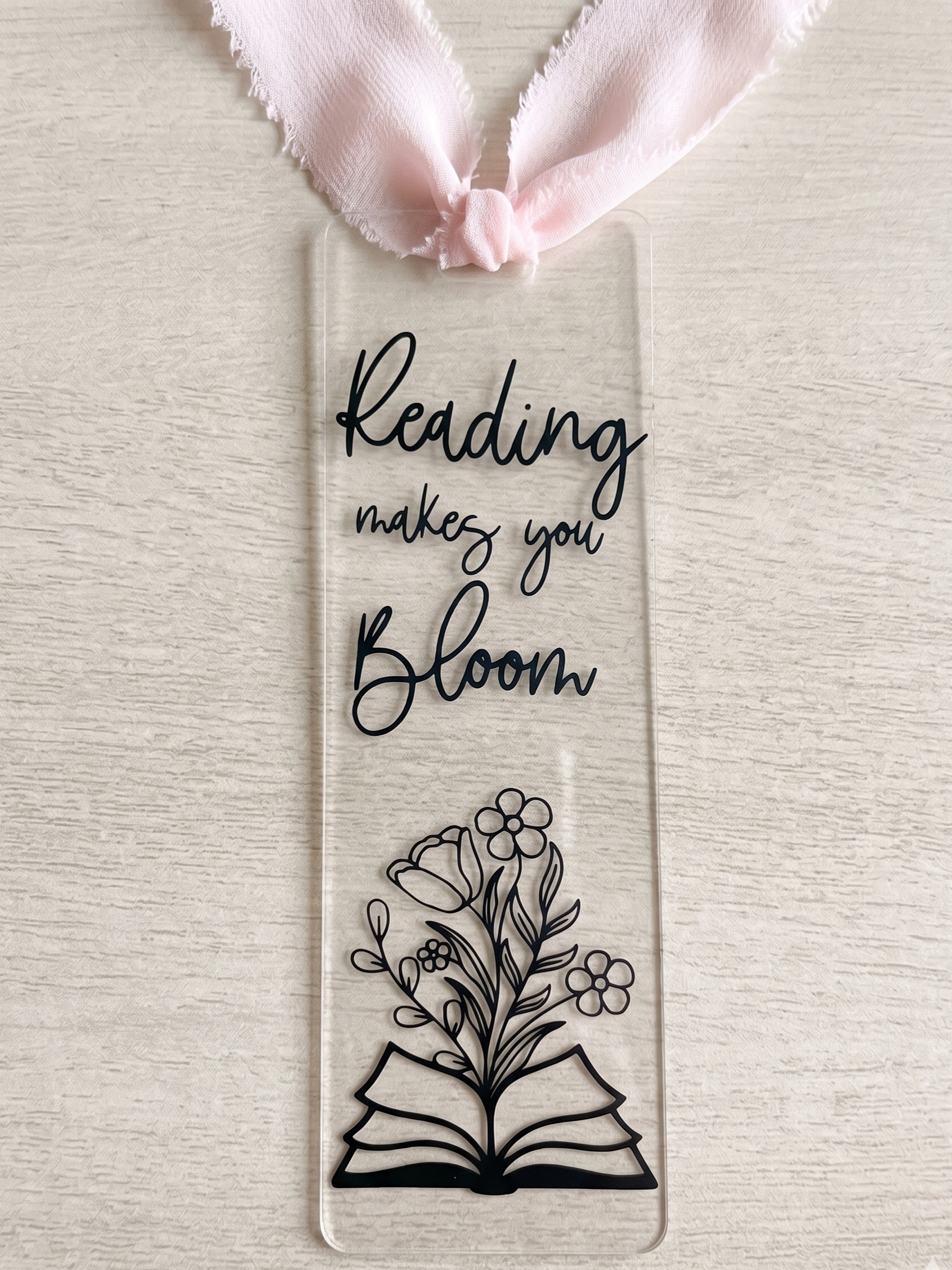 Reading makes you bloom bookmark with black lettering and light pink ribbon