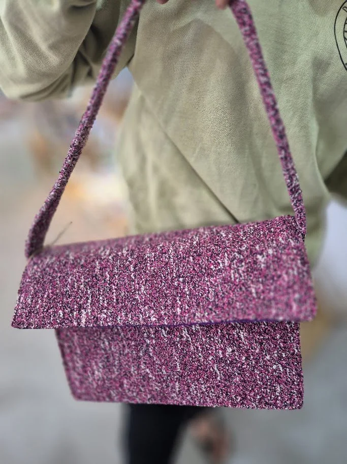 A pink glittery crossbody purse worn over a beige jacket, with part of a person's body visible.